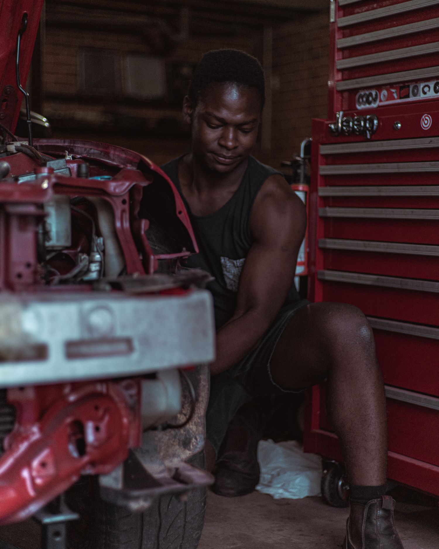 Black mechanic working on a car beside a red tool cabinet